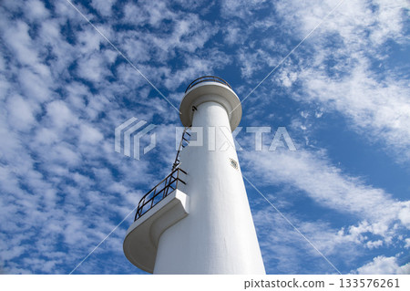 A white lighthouse towering against a blue sky shrouded in cirrocumulus clouds 133576261