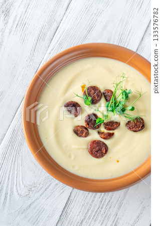 Creamy cauliflower soup with spicy chorizo served warmly in terracotta bowl on white table Creamy cauliflower soup with spicy chorizo served warmly in terracotta bowl on white table 133576782