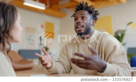 Black man speaking confidently during a strategy meeting with a white female colleague in a minimalist office 133576927