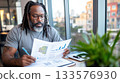 Black man in coworking lounge reviewing an ESG report with detailed graphics, with a city view 133576930