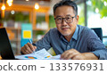 Asian male board member reviewing documents during corporate strategy session with laptop and esg dashboard 133576931