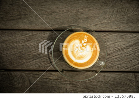 Latte art displayed in a glass cup on a wooden surface 133576985