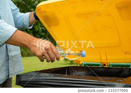 Person recycling a water bottle in a yellow trash bin Person recycling a water bottle in a yellow trash bin 133577000