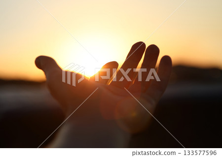 A hand reaching out toward the brightly rising sun, a New Year's sunrise background filled with hope for a brighter tomorrow and hopes and aspirations. A hand reaching out toward the brightly rising sun, a New Year's sunrise background filled with hope for a brighter tomorrow and hopes and aspirations. 133577596