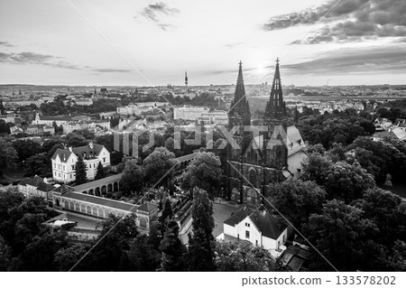 Morning light dances on the iconic Vysehrad Basilica of St. Peter and St. Paul. The historic site stands majestically against the backdrop of Prague's skyline, surrounded by lush greenery. 133578202