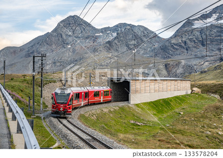 A red train travels along the Bernina railway line near the Bernina Pass. Majestic alpine mountains tower in the background, showcasing the stunning scenery of Graubunden. A red train travels along the Bernina railway line near the Bernina Pass. Majestic alpine mountains tower in the background, showcasing the stunning scenery of Graubunden. 133578204