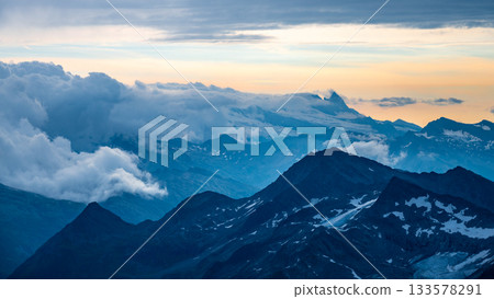Rocky alpine mountains morning panorama. Cloudy sunrise on summer day. Grossglockner Mountain, Hohe Tauern National Park, Austrian Alps Rocky alpine mountains morning panorama. Cloudy sunrise on summer day. Grossglockner Mountain, Hohe Tauern National Park, Austrian Alps 133578291