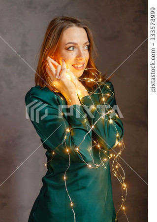 Portrait of a young woman celebrating Christmas Eve. Model posing for a photo. Woman wearing green dress. Portrait of a young woman celebrating Christmas Eve. Model posing for a photo. Woman wearing green dress. 133578999