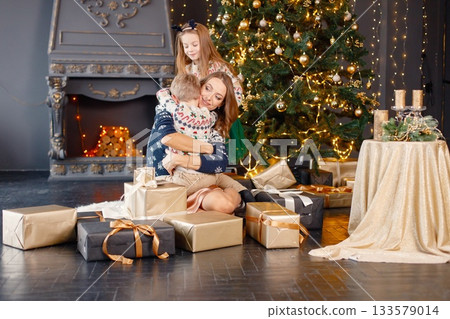 Young mother, little daughter and son in studio posing for a photo. Woman and kids wearing knitted sweaters with Christmas prints. Mother hugging her son. 133579014