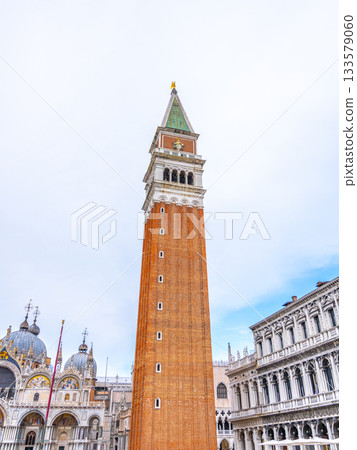 The Campanile di San Marco stands majestically in the heart of Venice, Italy, surrounded by stunning architecture and the ambiance of a bustling square during the day. 133579060