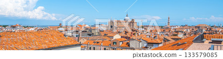 A stunning aerial perspective highlights the unique rooftops and architecture of Venice, Italy, showcasing the city's charm against a backdrop of blue skies and scattered clouds. 133579085