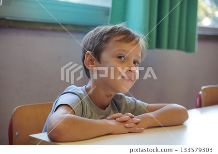 Smiling Boy at School Desk with Hands Folded 133579303