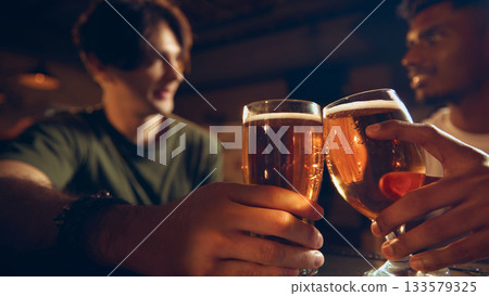 Closeup of beer glasses in hands during friendly toast at pub counter 133579325