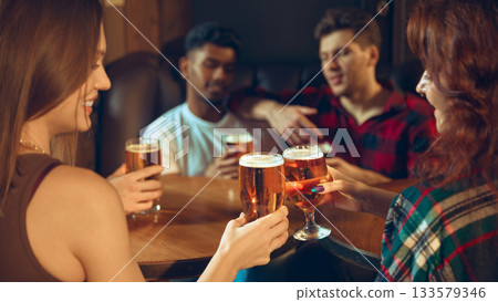 Friends toasting beer glasses with warm light on pub table 133579346