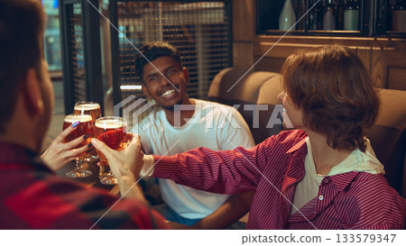 Friends cheering beer glasses across table in relaxed bar corner 133579347