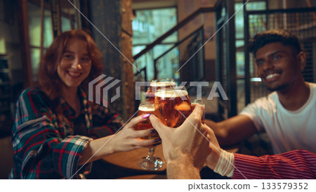 Group raising beer glasses around pub table in warm interior 133579352