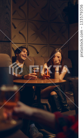 Couple laughing with beer mugs in intimate pub corner 133579356