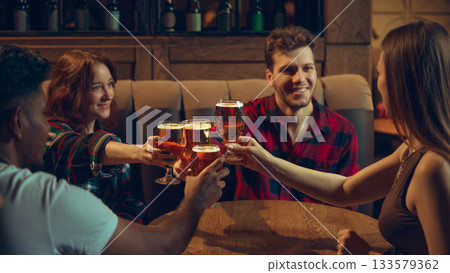 Friends clinking beer glasses in relaxed tavern setting Friends clinking beer glasses in relaxed tavern setting 133579362