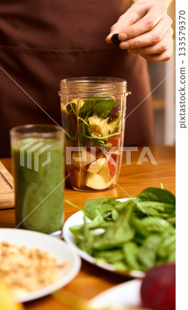 Close-up of blender jar filled with fruit and greens beside glass of green smoothie 133579370