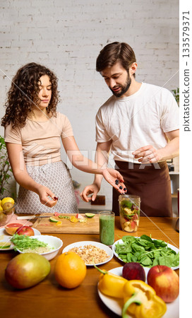 Couple adding berries and fruit into blender jar while preparing healthy smoothies Couple adding berries and fruit into blender jar while preparing healthy smoothies 133579371