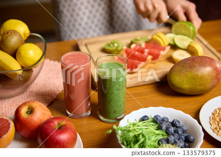 Fresh fruit being sliced beside two glasses of pink and green smoothies on wooden table Fresh fruit being sliced beside two glasses of pink and green smoothies on wooden table 133579375