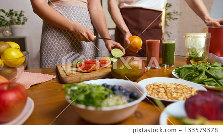 Slicing citrus and kiwi while smoothies stand among fresh produce on table Slicing citrus and kiwi while smoothies stand among fresh produce on table 133579378