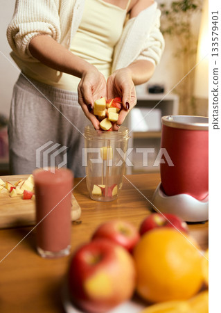 Hands placing chopped apples into blender cup while preparing fresh smoothie 133579401