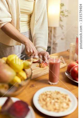 Hands cutting fresh apples for homemade smoothie with ingredients arranged on table 133579404