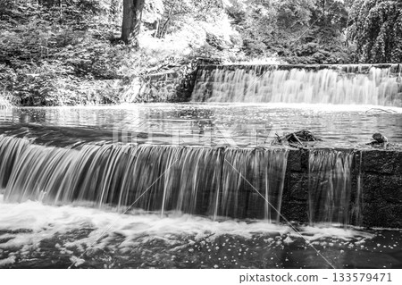 Small double waterfall on the forest stream. Gaden stone sluice in tranquil forest mood. Black and white image. Small double waterfall on the forest stream. Gaden stone sluice in tranquil forest mood. Black and white image. 133579471