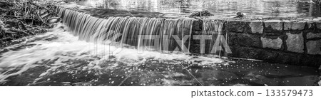 Small waterfall on the forest stream. Gaden stone sluice in tranquil forest mood. Black and white image. 133579473