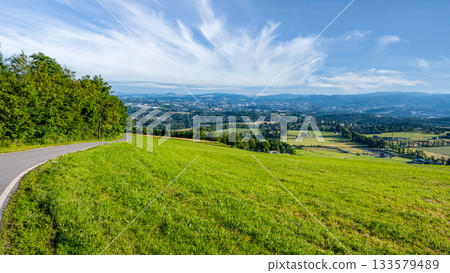From the heights of Javornik, Liberec City unfolds below, revealing lush greenery, rolling hills, and a captivating skyline under a clear blue sky. A peaceful setting invites exploration. 133579489