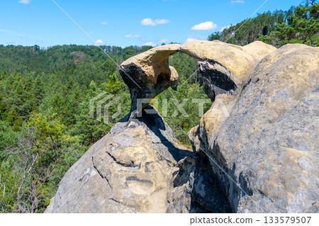 Unique sandstone arch in pine forest on dry sunny summer day. Bohemian Paradise, Czech Republic 133579507