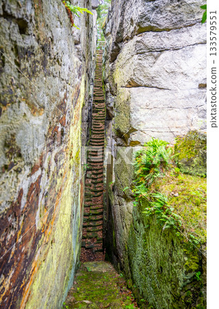 Visitors navigate the steep, narrow staircase surrounded by towering rock formations at the Sloup v Cechach castle ruins in Czechia, experiencing the historical charm and natural beauty. Visitors navigate the steep, narrow staircase surrounded by towering rock formations at the Sloup v Cechach castle ruins in Czechia, experiencing the historical charm and natural beauty. 133579551