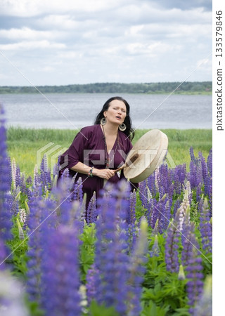 Shaman woman drumming among blooming flowers 133579846