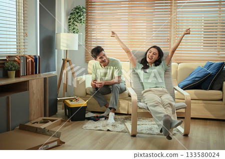 Happy couple celebrating after finishing furniture assembly, success in DIY home project Happy couple celebrating after finishing furniture assembly, success in DIY home project 133580024