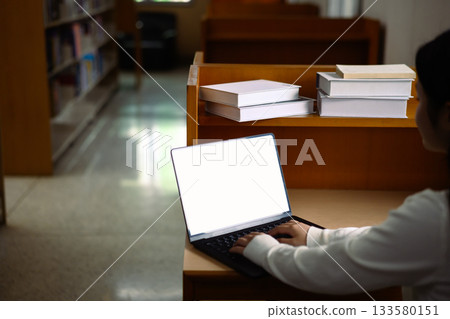 Hands holding mockup laptop in library 133580151