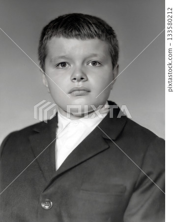 A vintage portrait of a serious-looking schoolboy wearing a jacket and white shirt. Retro photo from the 1969. A vintage portrait of a serious-looking schoolboy wearing a jacket and white shirt. Retro photo from the 1969. 133580212