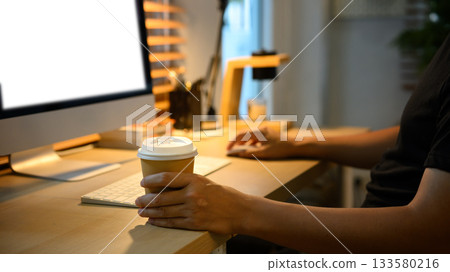 Closeup man coffee cup while working on computer at cozy home office desk, warm light 133580216