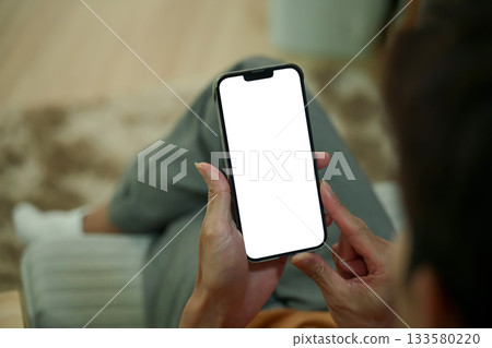 Close up of man hands holding a smartphone with white screen sitting on armchair Close up of man hands holding a smartphone with white screen sitting on armchair 133580220