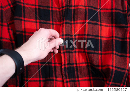 Buttoning a red plaid shirt Buttoning a red plaid shirt 133580327