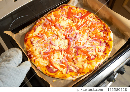 Ready Pizza with Cheese and Vegetables Taken Out of Oven in Mitt 133580328