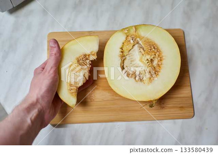 Hand-Cutting Ripe Melon on Wooden Cutting Board 133580439