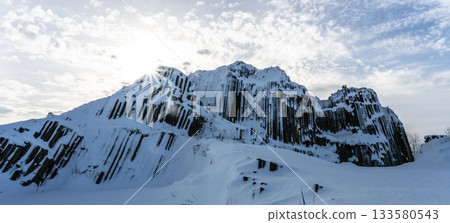 Panska skala - rock formation of pentagonal and hexagonal basalt columns. Looks like giant organ pipes. Covered by snow and ice in winter time. Kamenicky Senov, Czech Republic. Panska skala - rock formation of pentagonal and hexagonal basalt columns. Looks like giant organ pipes. Covered by snow and ice in winter time. Kamenicky Senov, Czech Republic. 133580543