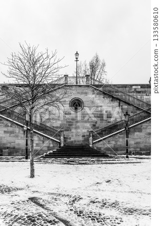 Historic stone staircase leading from Kampa Island to Charles Bridge in Prague, Czech Republic. The winter scenery adds to the picturesque view. Black and white photography. Historic stone staircase leading from Kampa Island to Charles Bridge in Prague, Czech Republic. The winter scenery adds to the picturesque view. Black and white photography. 133580610