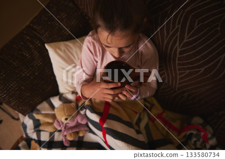 Young Child Sits Cozy On Couch Holding Wooden Cup, Warm Blanket And Plush Bear Nearby Young Child Sits Cozy On Couch Holding Wooden Cup, Warm Blanket And Plush Bear Nearby 133580734