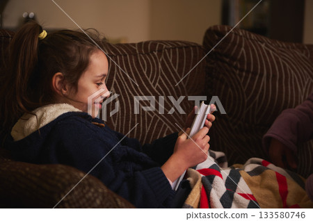 Young Girl Relaxing On Couch With Blanket, Looking at Cards In Cozy Home Setting 133580746