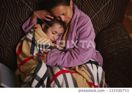 Mother And Child Cuddling On Couch, Warm Blanket, Gentle Nighttime Embrace 133580753