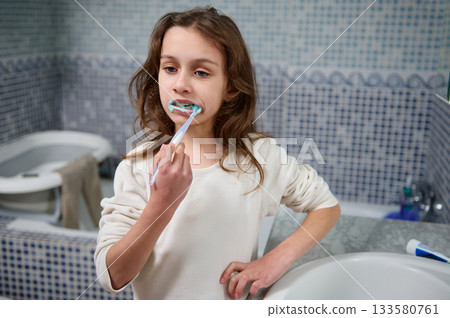 Young Girl Brushing Teeth in Bathroom Mirror During Morning Routine Young Girl Brushing Teeth in Bathroom Mirror During Morning Routine 133580761