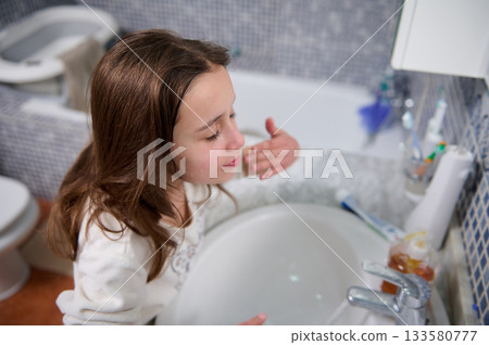 Young Girl At Bathroom Sink Washing Face In A Calm Family Moment 133580777