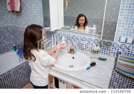 Young Girl Washing Hands At Marble Bathroom Sink With Blue Mosaic Tiles And Mirror 133580790